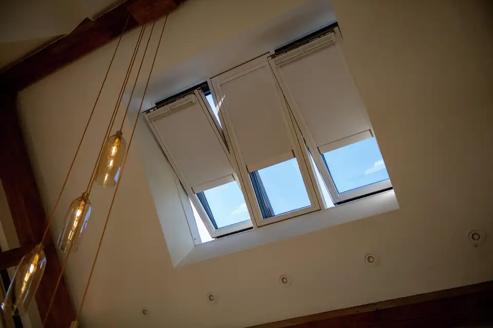 Een gekanteld zicht op een plafond met drie rechthoekige dakramen, waardoor natuurlijk licht de kamer binnenkomt. De hoek en compositie creëren een interessant perspectief en spelen met de architecturale lijnen en het natuurlijke licht.