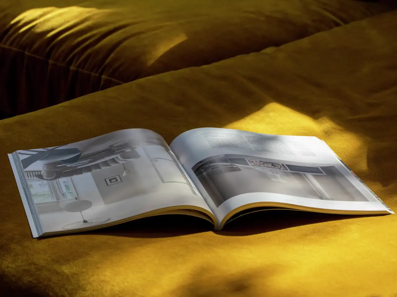 Offene Zeitschrift auf goldener Samtoberfläche im Sonnenlicht, die Innenarchitektur präsentiert.