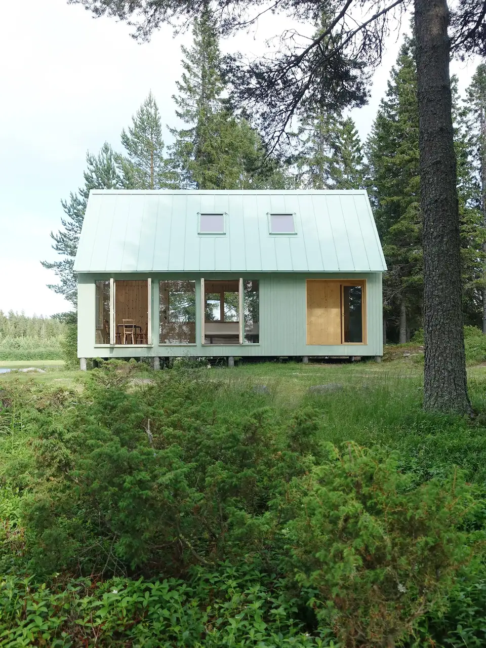 Moderne sommerhus i skovmiljø med store vinduer, der åbner op til naturen