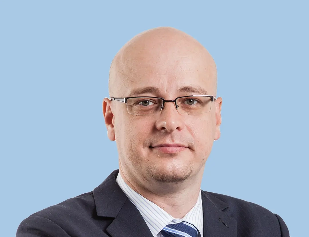 Man in a dark suit with a striped tie against a blue background.
