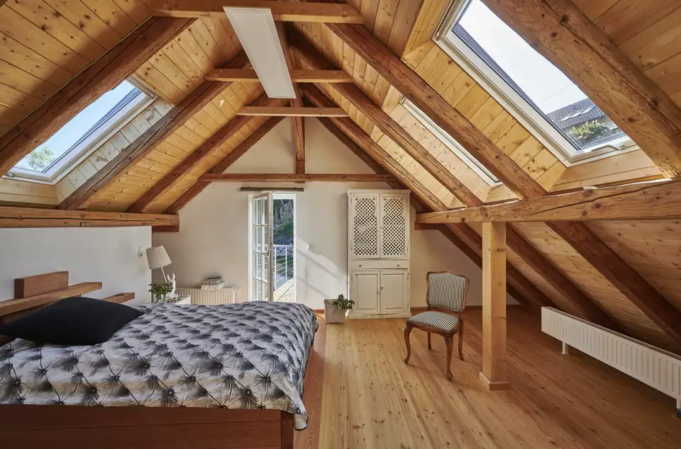 Camera da letto in mansarda con soffitto in legno e due finestre per tetti su pareti opposte