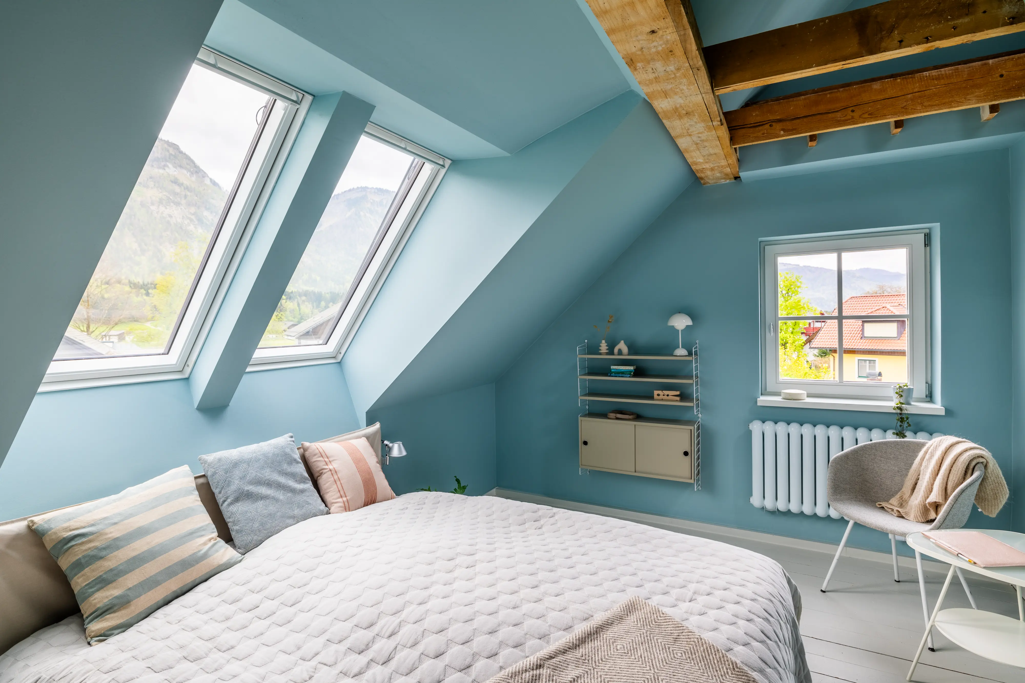 Palėpės miegamasis su nuožulniomis lubomis, VELUX langais ir vaizdu į kalnus.