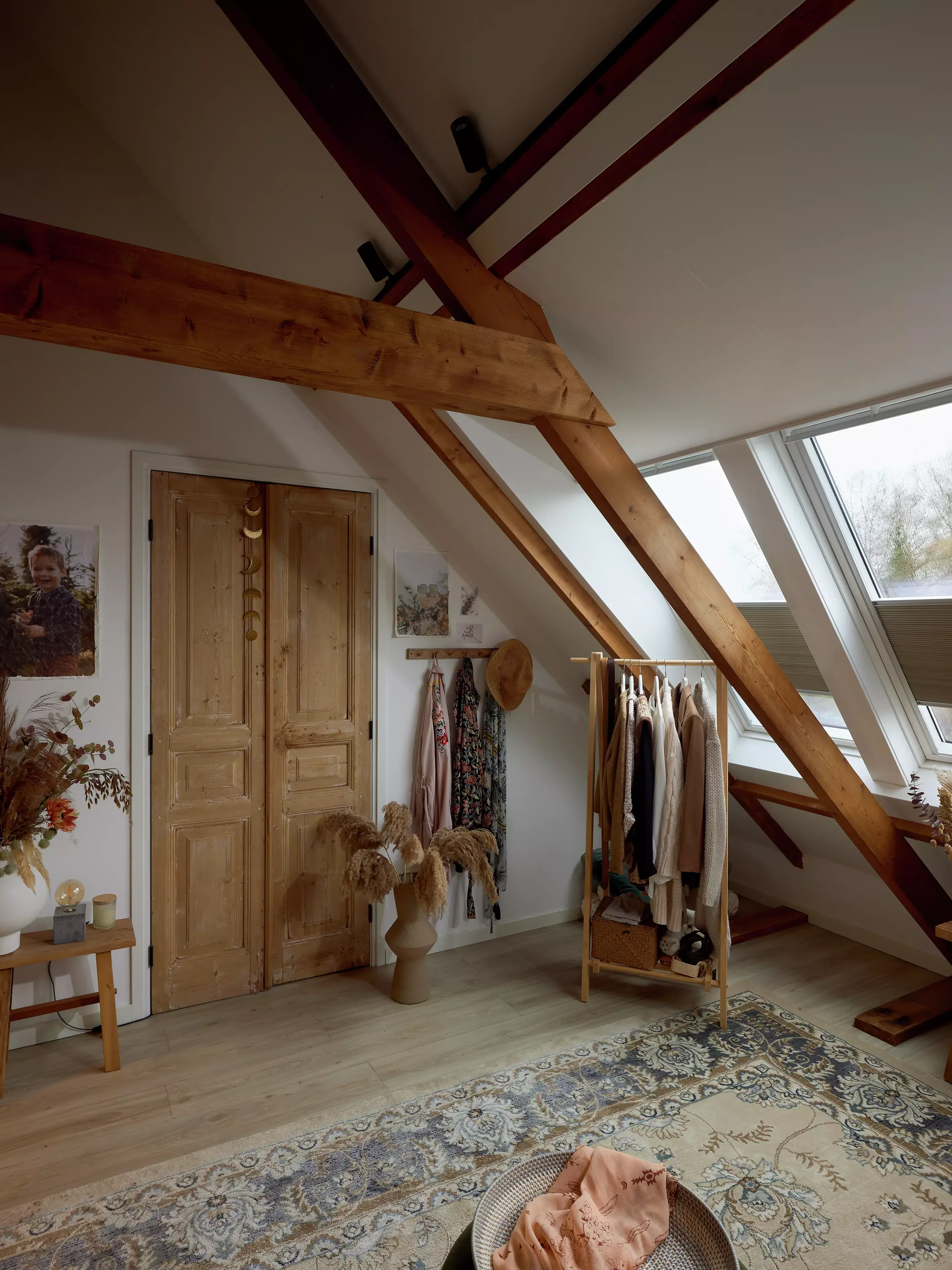 Chambre mansardée rustique avec des poutres en bois et une fenêtre de toit VELUX, une armoire vintage et un tapis à motifs.