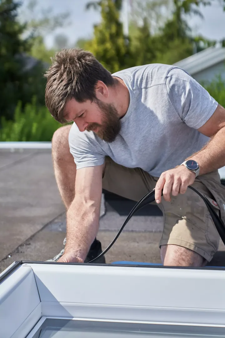 Junger Handwerker in Arbeitskleidung während einer Flachdachsanierung | VELUX Magazin