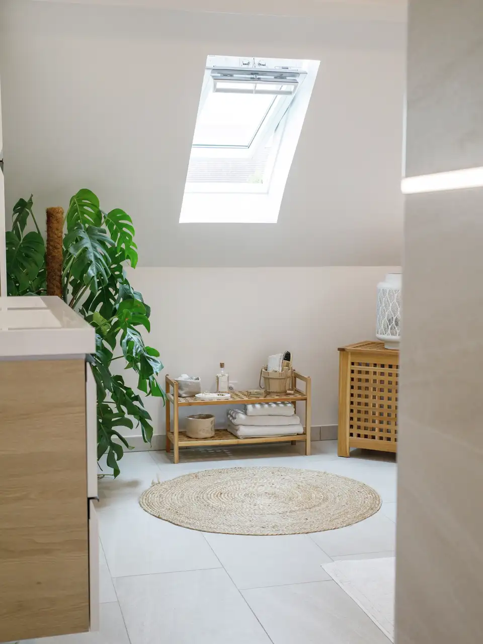 Salle de bains moderne avec grands carreaux gris au sol et au mur, mobilier minimaliste et lumière naturelle par fenêtres de toit.