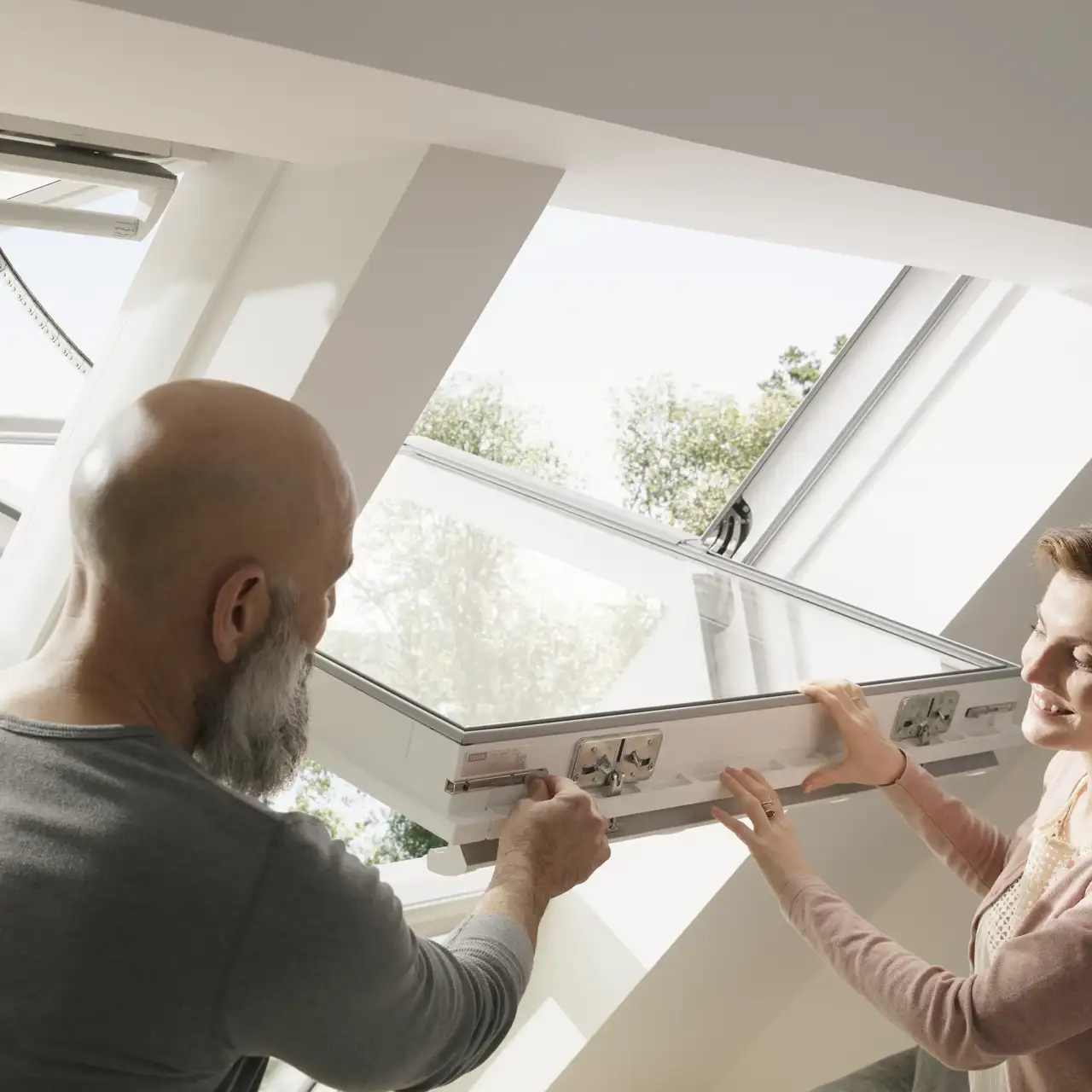 installateur et propriétaire ajustant une nouvelle fenêtre de toit VELUX dans une pièce lumineuse