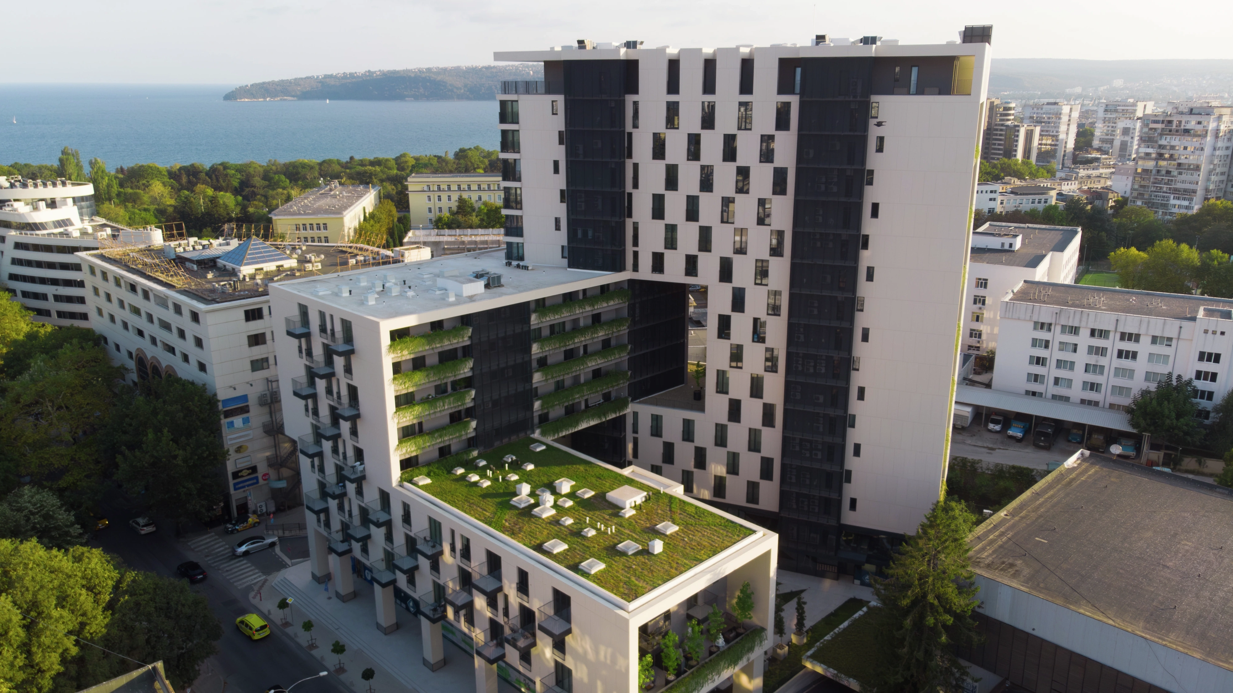 Modern apartment complex with large green flat roof and sea in the background.