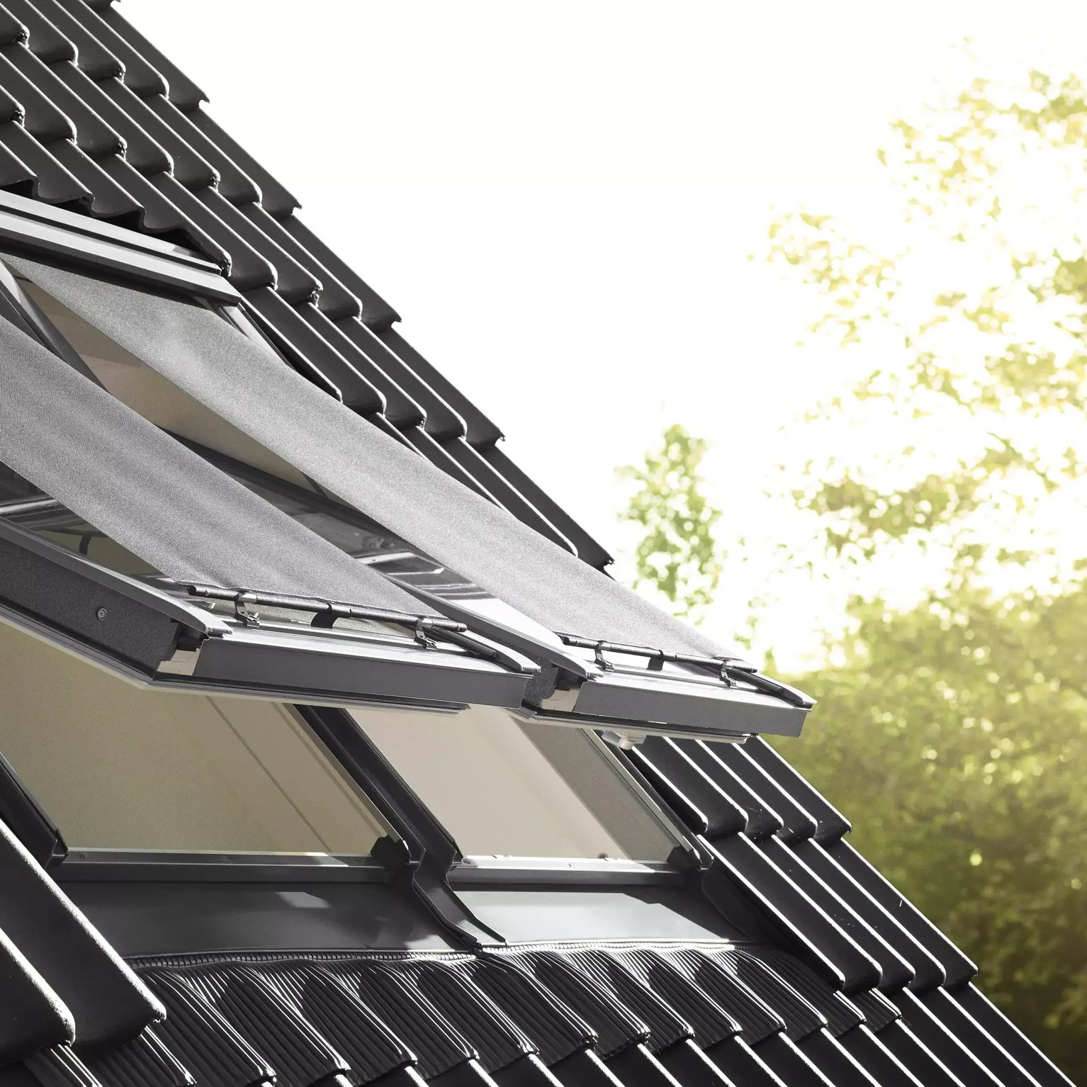 Modern roof with black tiles and open VELUX roof windows, sunlight streaming in.
