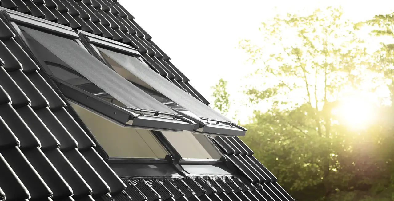 Toit en tuiles noires avec fenêtres de toit VELUX ouvertes et stores extérieurs anti-chaleur 