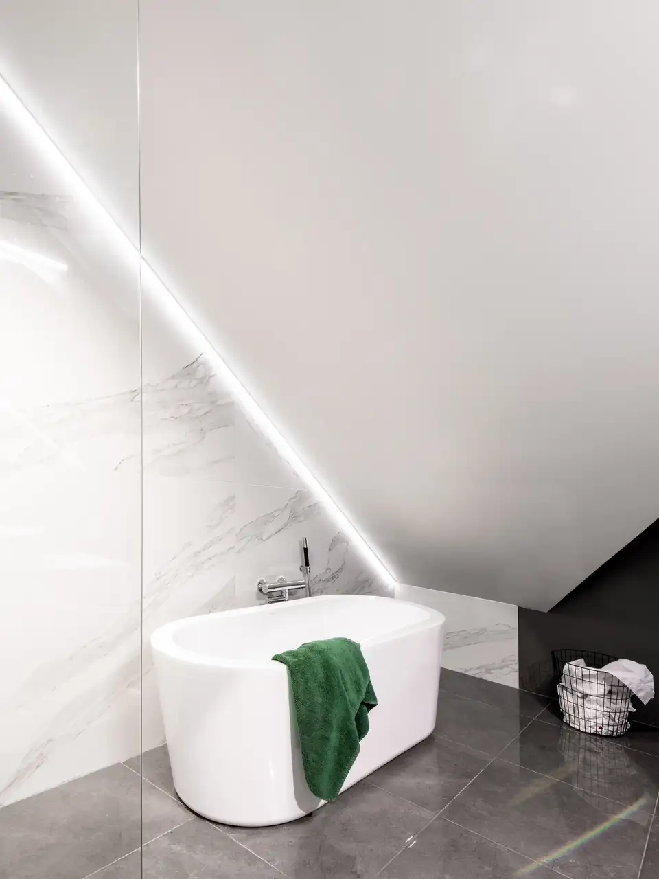  Salle de bain moderne sous les combles avec baignoire îlot et éclairage LED d’accent sur le mur incliné.