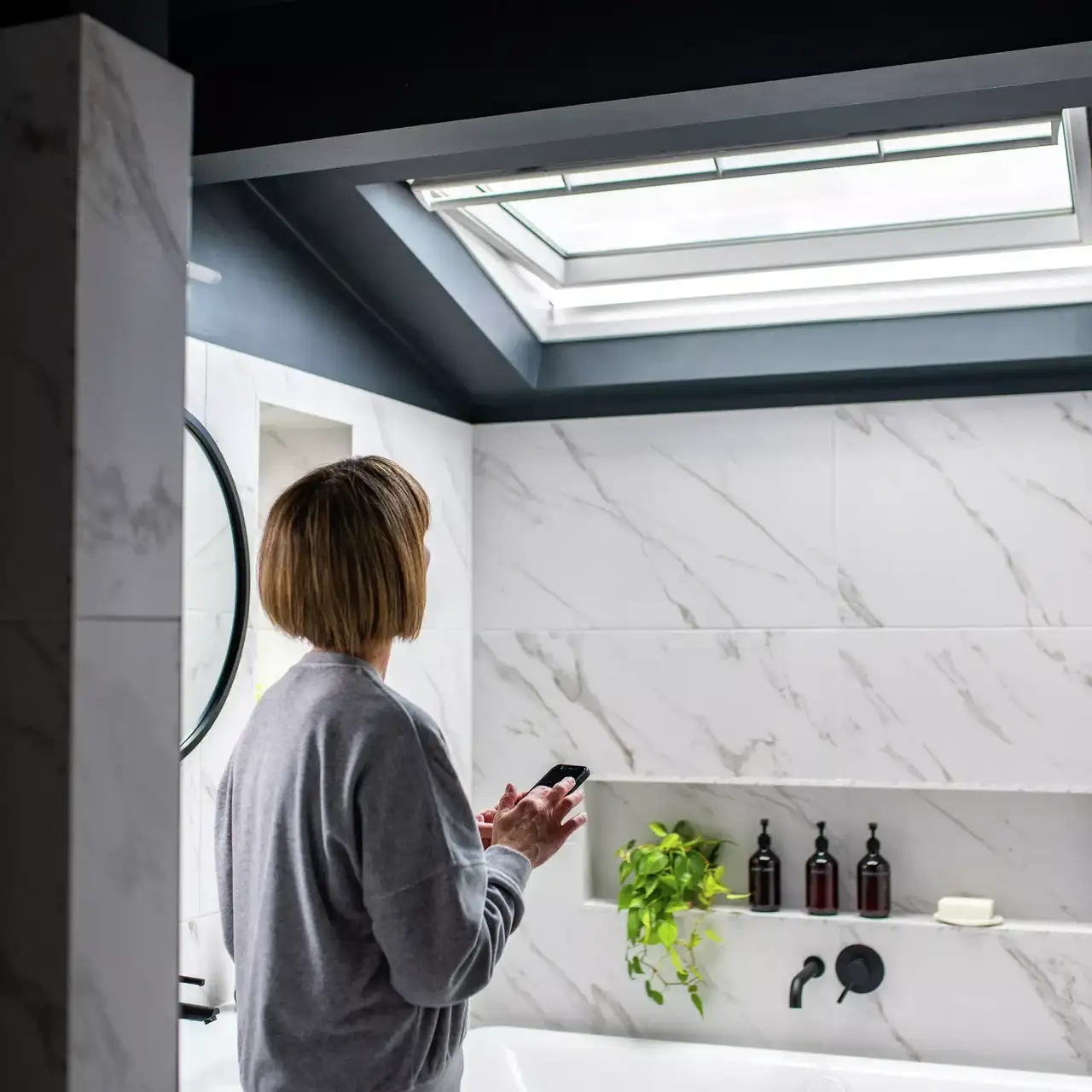 Frau in modernem Badezimmer mit Marmorwänden und VELUX Dachflächenfenster.