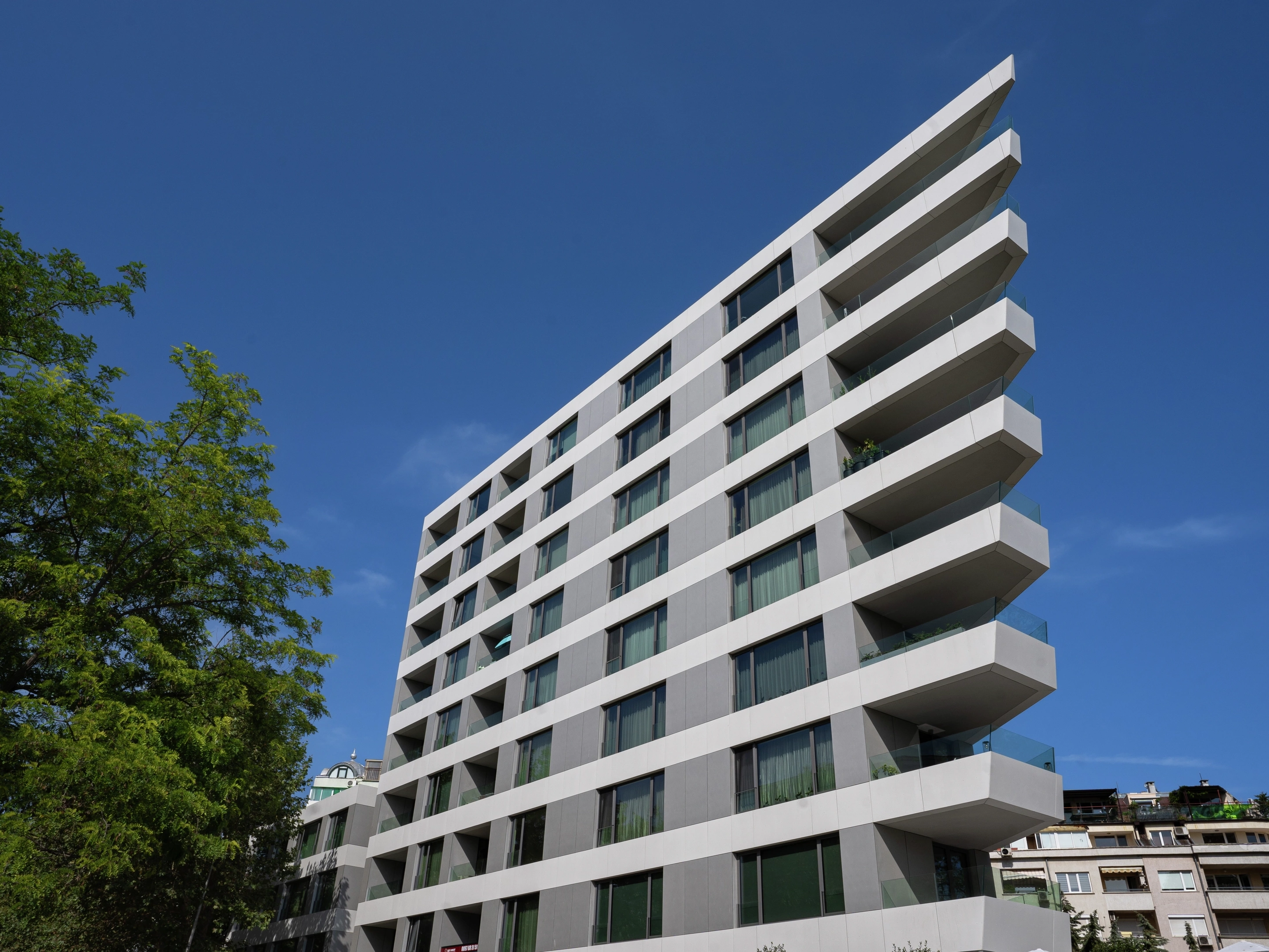 Angular white apartment building with long balconies under a clear blue sky.
