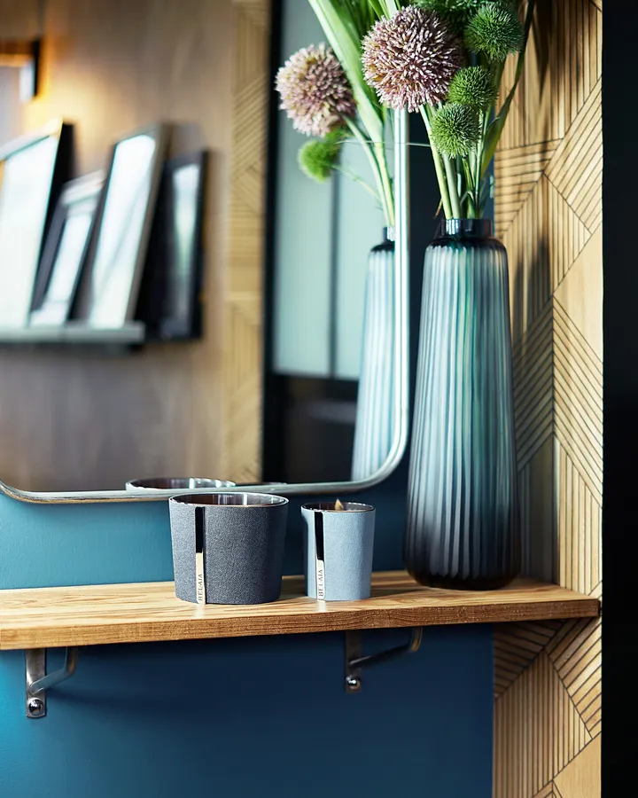 Geometrik desenli duvar önünde yer alan, Art Deco esintili raf; çizgili cam vazo ve şık dekoratif saksılarla tamamlanmış.