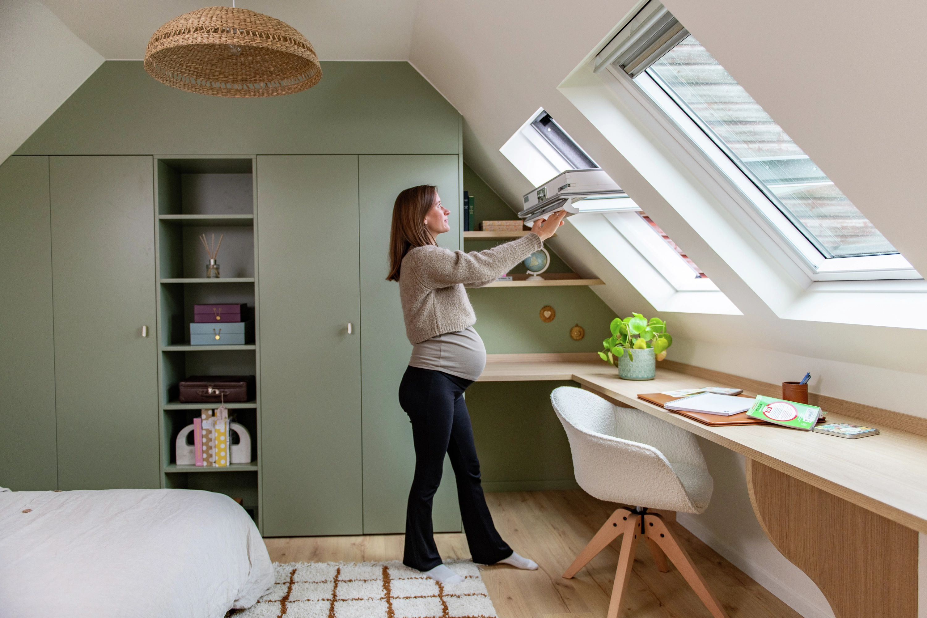 Femme enceinte ouvrant une fenêtre de toit VELUX dans une chambre rénovée et lumineuse