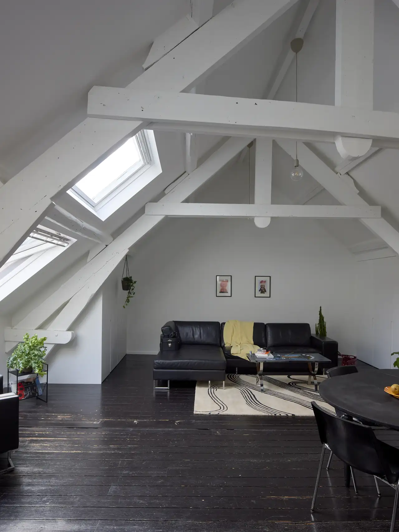 Mansarda con soffitto spiovente e travi a vista bianche, pavimento in parquet scuro e due finestre per tetti sovrapposte.