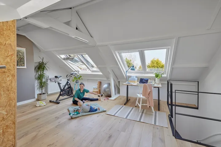 Таванско помещение със скосен таван, прозорци VELUX, бюро и кът за упражнения.