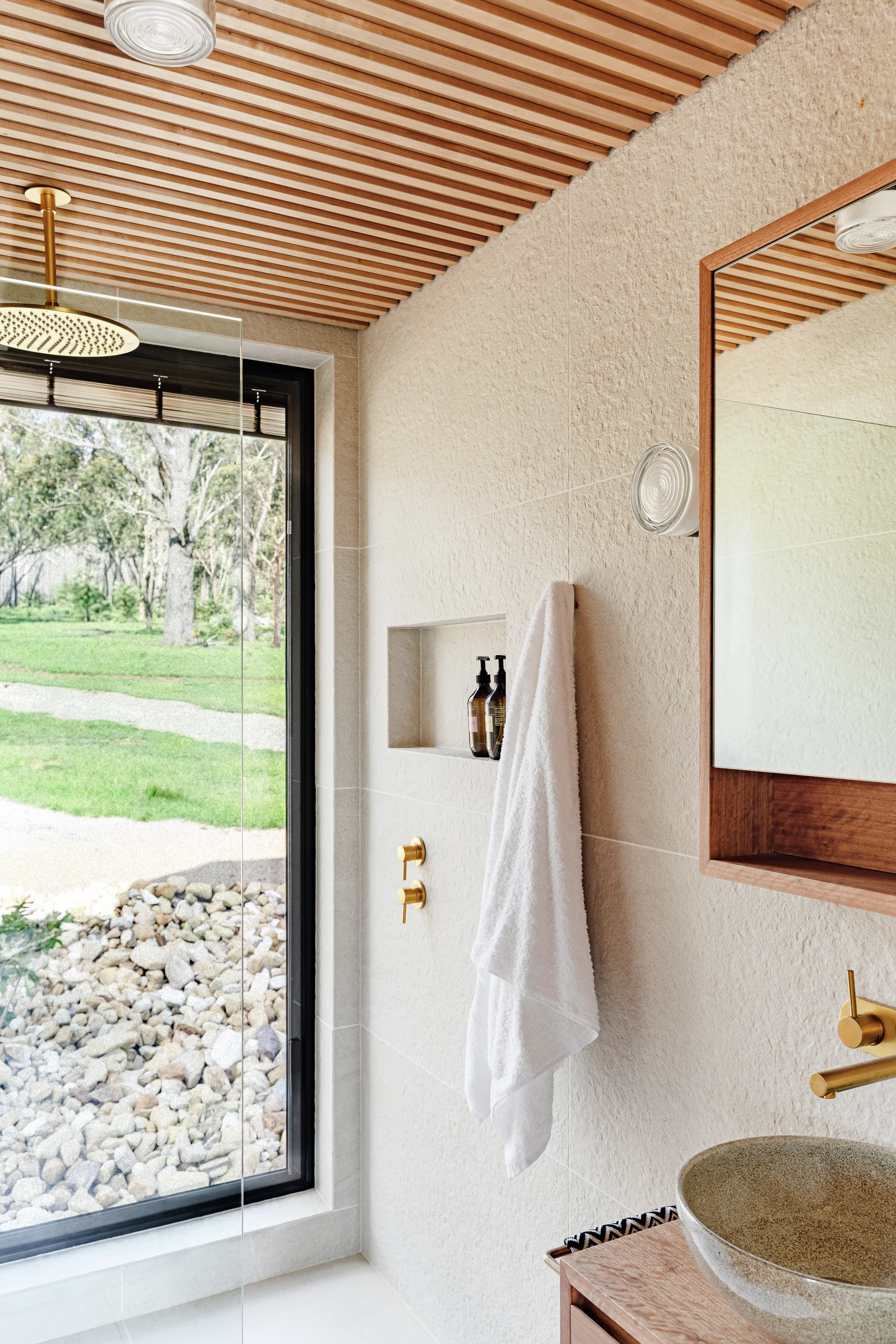 Modern shower bathroom with large window, brass fixtures and garden view.