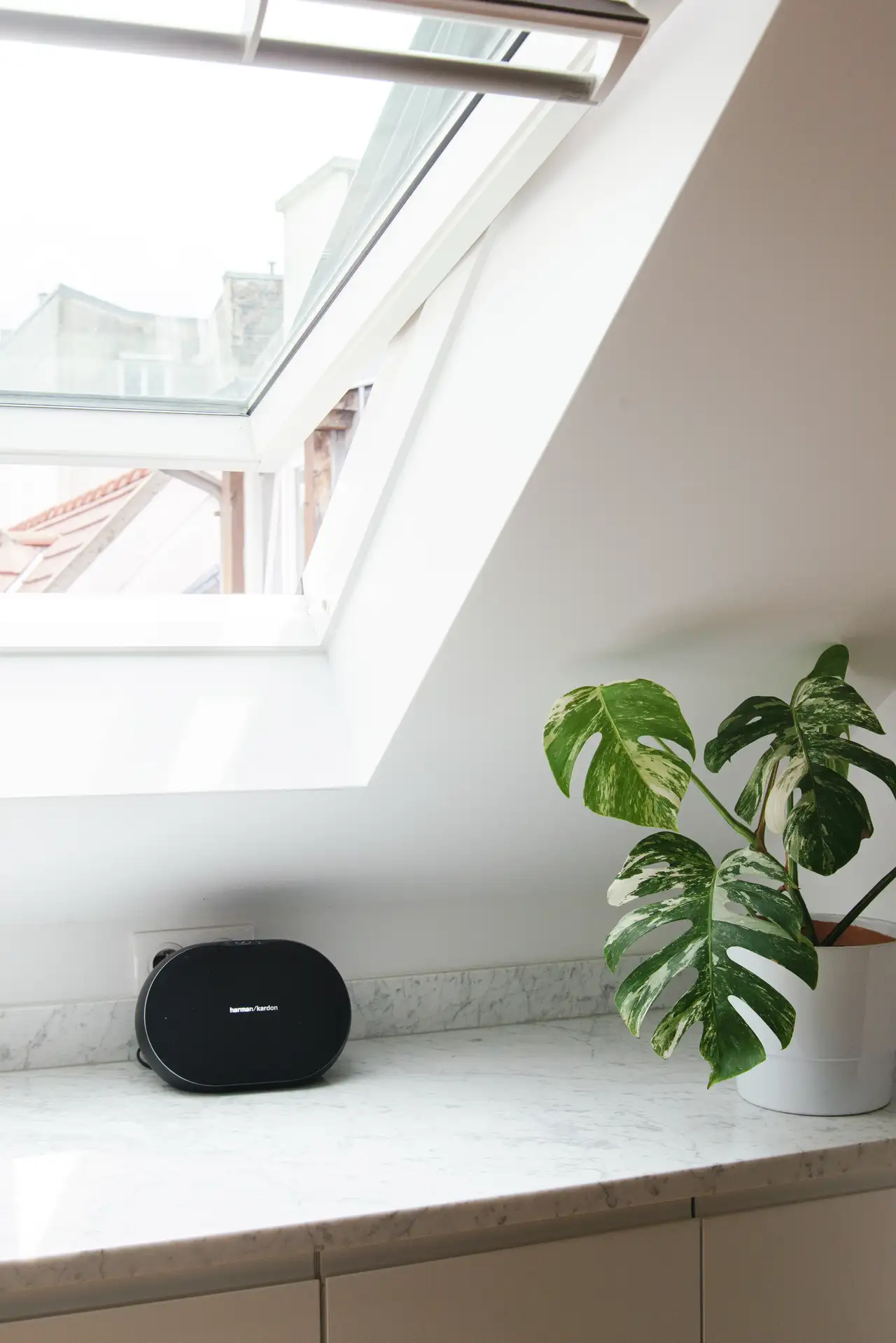 Atvērta jumta loga tuvplāns virs virtuves letes ar zaļu podaugu un melnu skaļruni. | VELUX