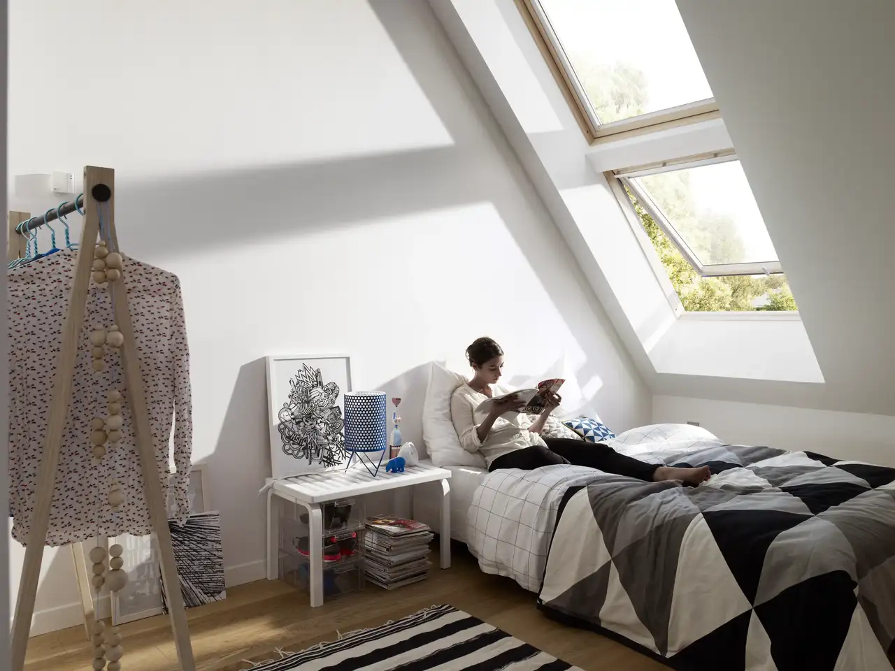  Una donna legge una rivista sul suo letto sotto due finestre per tetti VELUX sovrapposte.