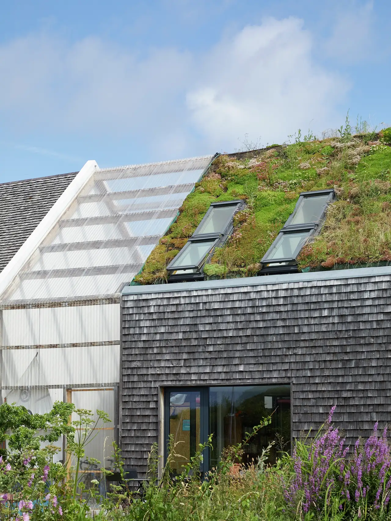 Vivienda con fachada de pizarra y cristal y ventanas de tejado en cubierta con jardín.