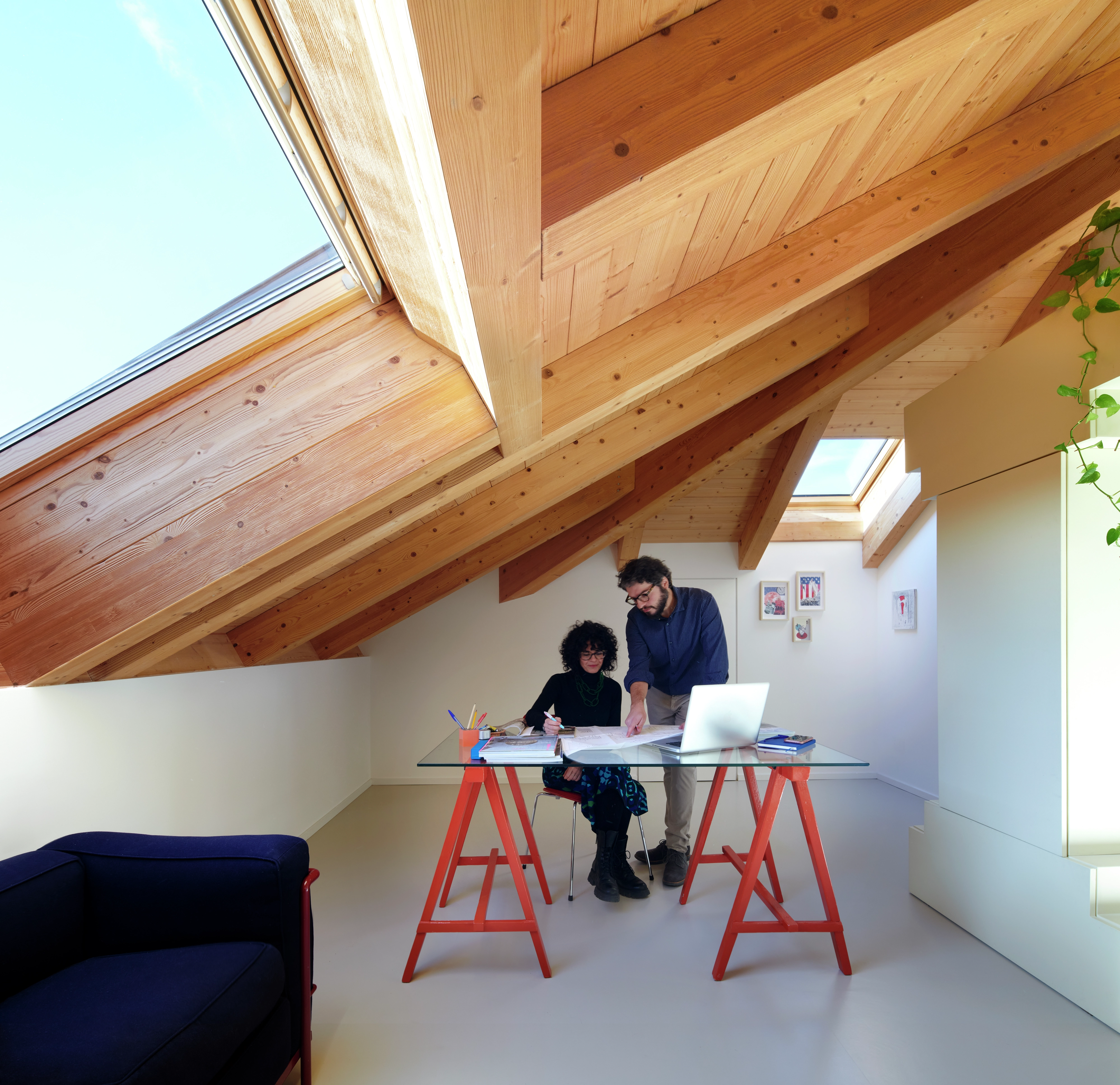 Ufficio domestico mansarda con travi in legno e finestra VELUX, scrivania moderna e decorazione minimalista.