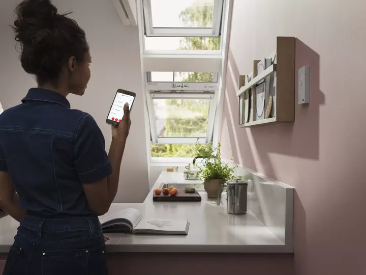 Frau bedient elektrisches Dachfenster per Sprachsteuerung mit ihrem Handy | VELUX Magazin