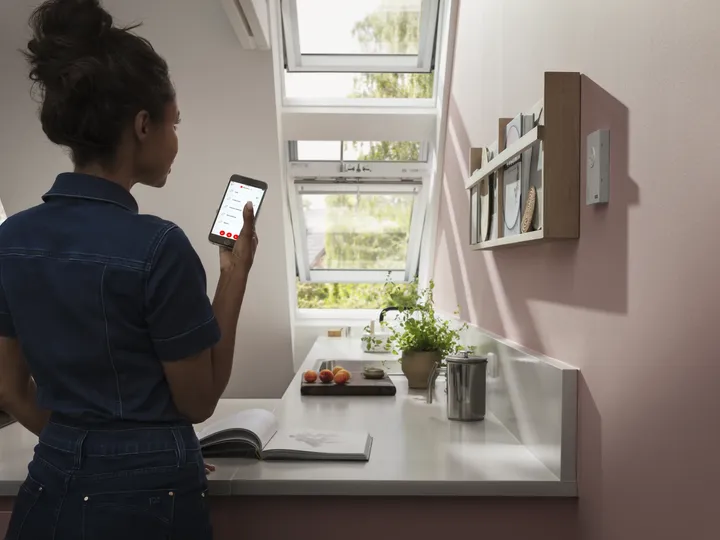 Frau bedient elektrisches Dachfenster per Sprachsteuerung mit ihrem Handy | VELUX Magazin