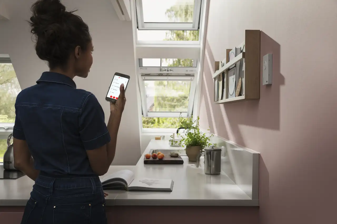 Jeune femme utilisant l’application VELUX App Control pour ouvrir deux fenêtres de toit dans une cuisine