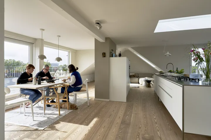 Moderne weiße Küche mit zentraler Insel und hölzernem Esstisch unter einem VELUX Dachflächenfenster.