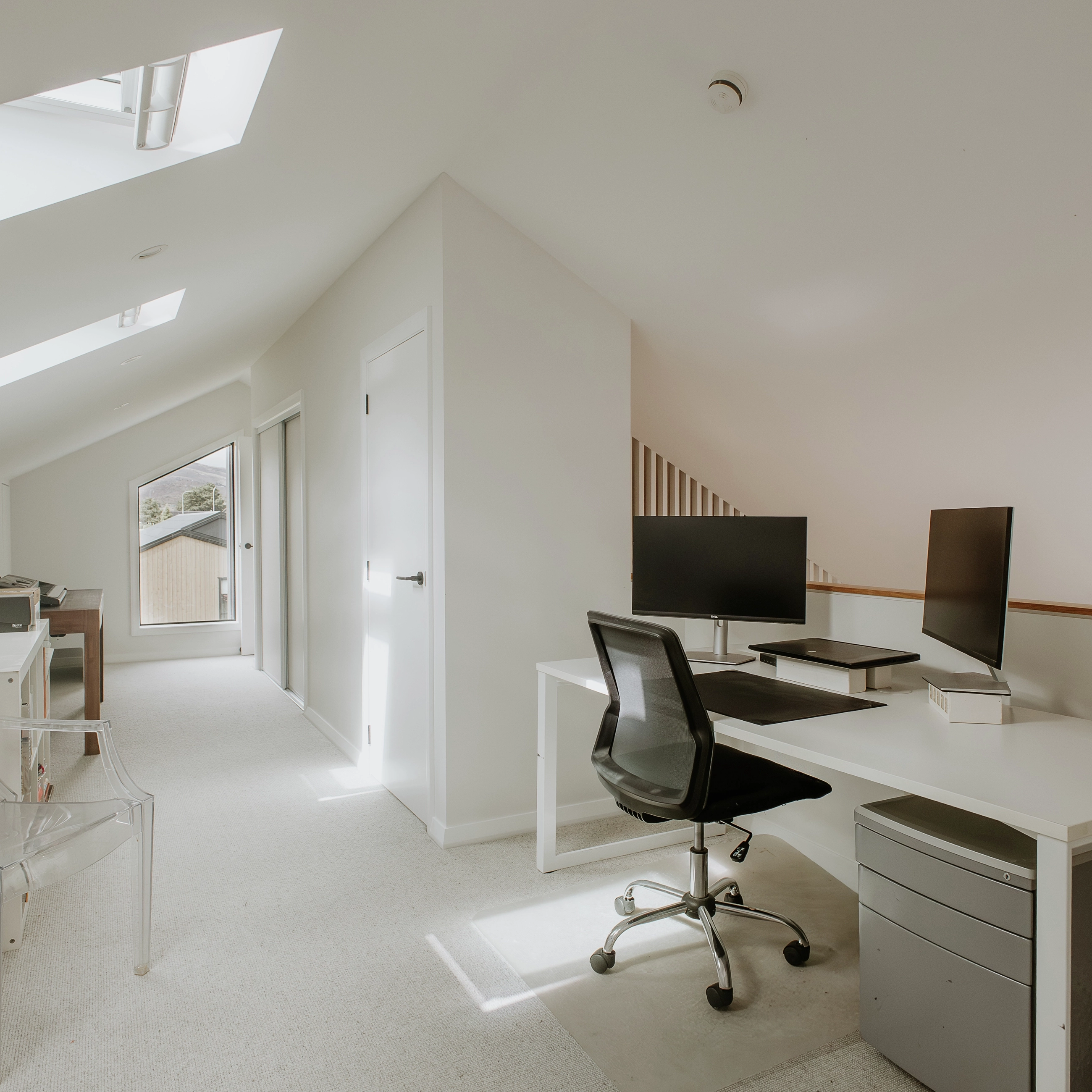 Minimal attic home office with VELUX roof windows and modern white desk.