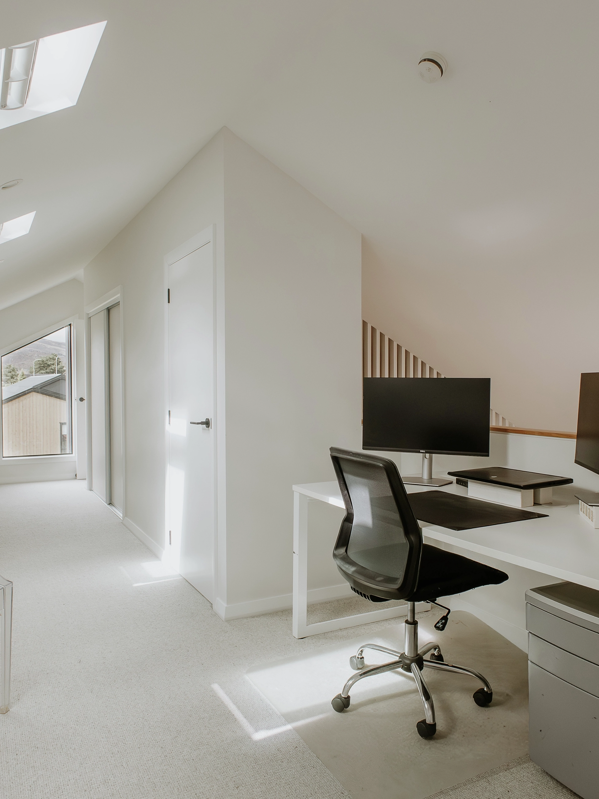 Minimal attic home office with VELUX roof windows and modern white desk.
