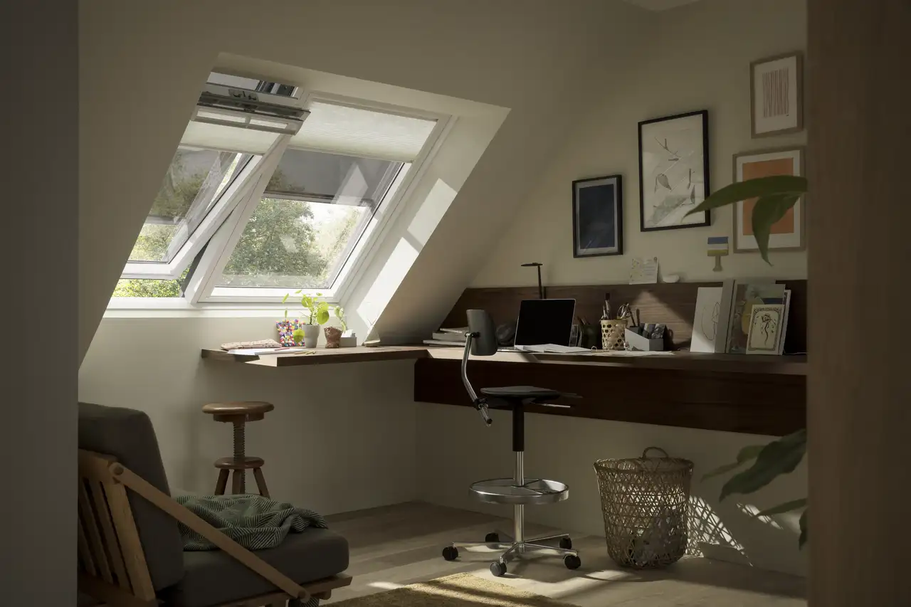 Mansarda con angolo studio compatto accanto a finestre per tetti, scrivania salvaspazio con pc e accessori.