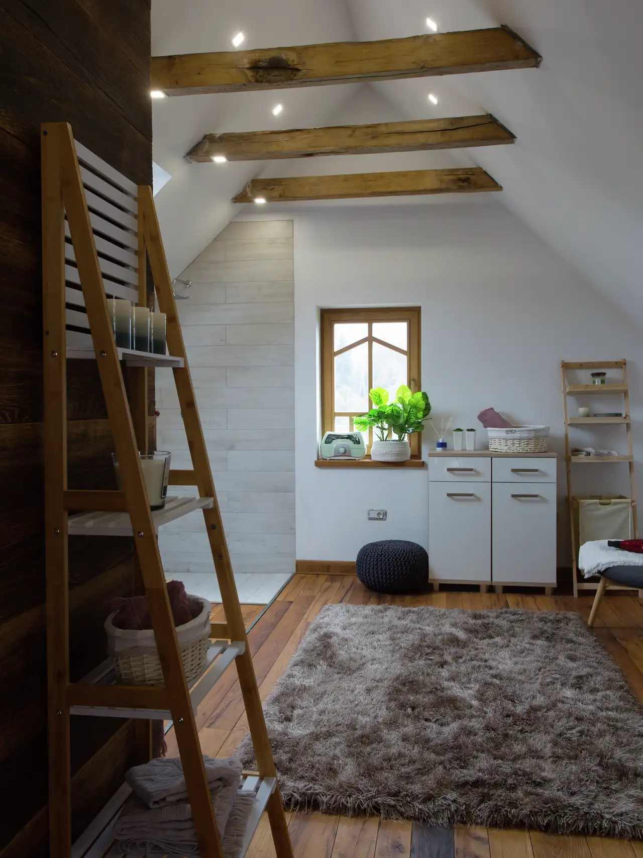 Mansarda con travi a vista con faretti sulle travi e sul soffitto inclinato.