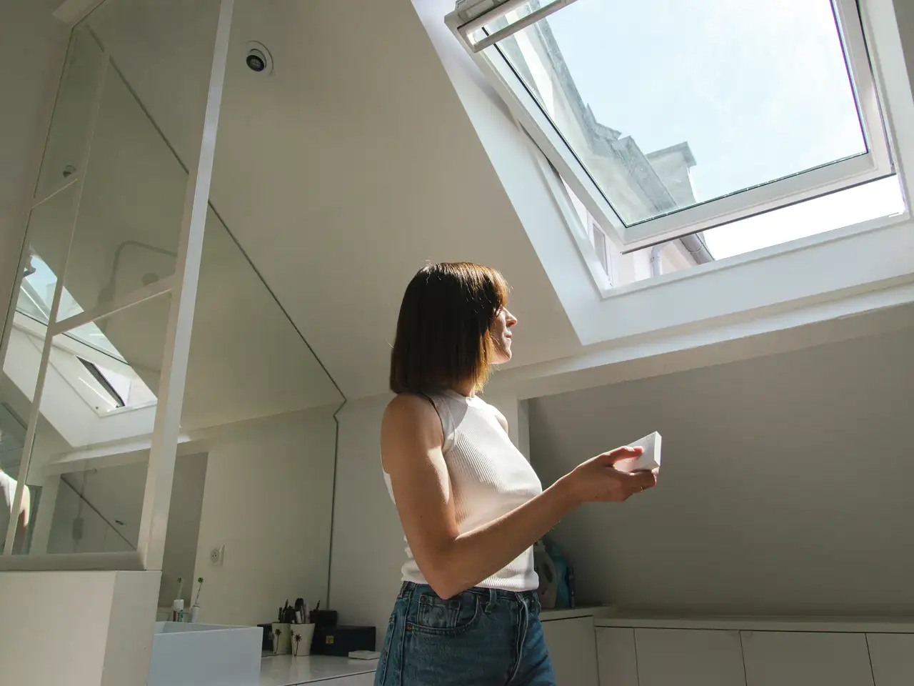 Moteris nuotolinio valdymo pulteliu valdo stogo langą šviesiame, šiuolaikiškame kambaryje. | VELUX 