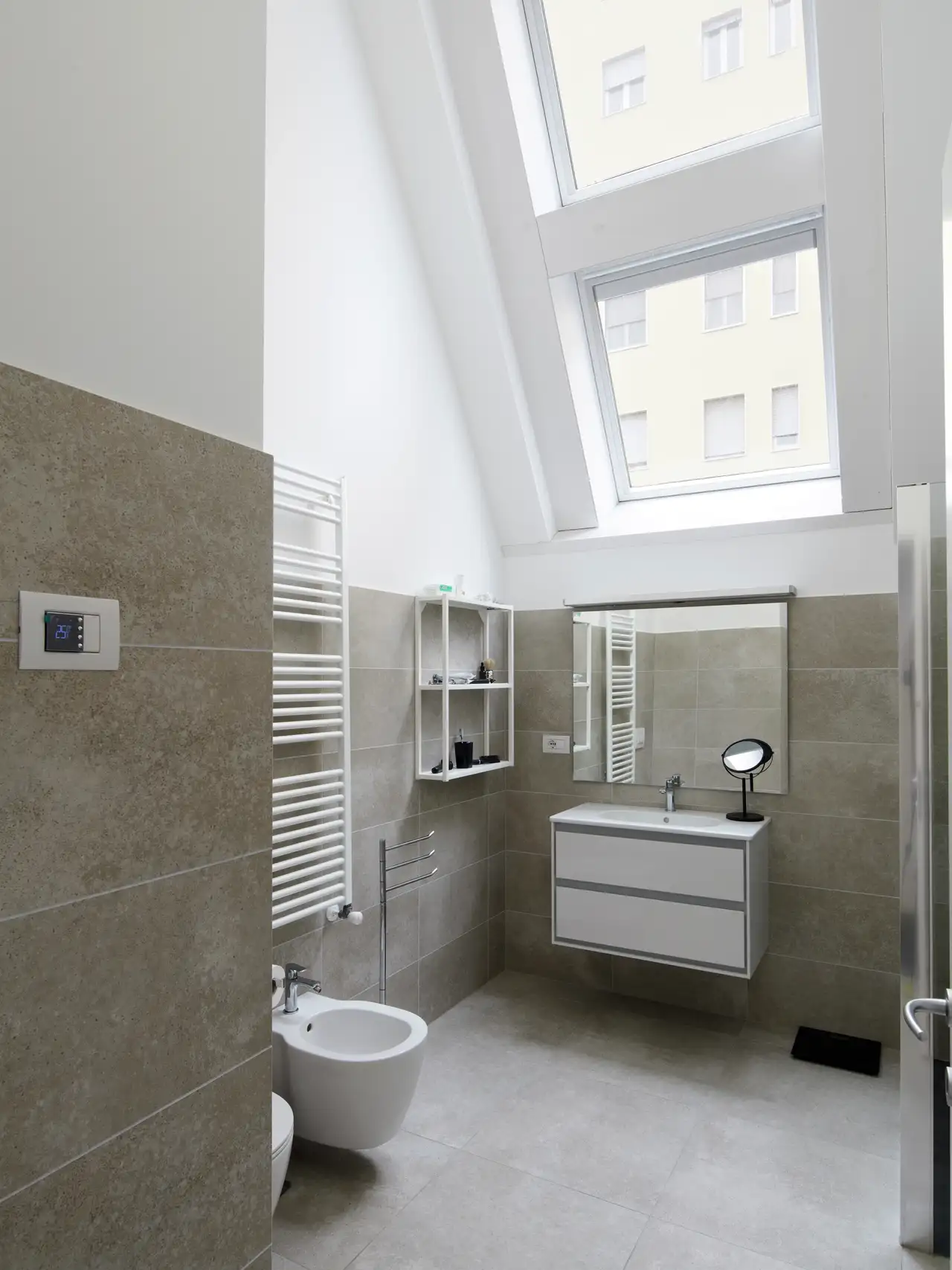 Bagno con WC, bidet, lavandino, specchio, mensole e finestre per tetti nel sottotetto.