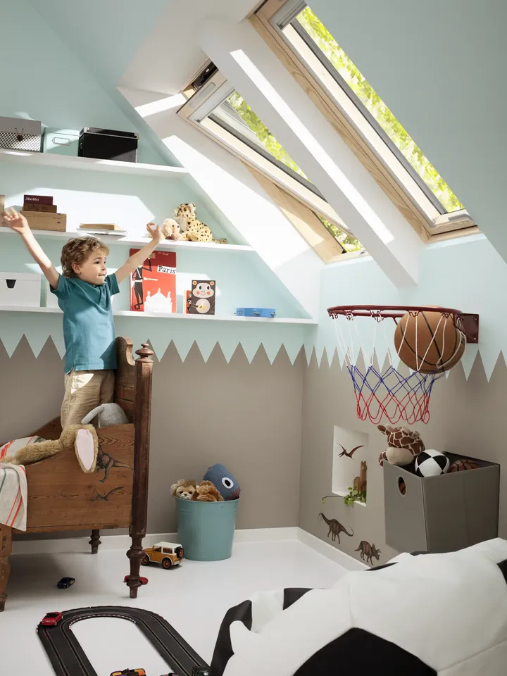 Kleiner Junge steht in seinem Kinderbett und schaut durch die gekippten Dachfenster | VELUX Magazin