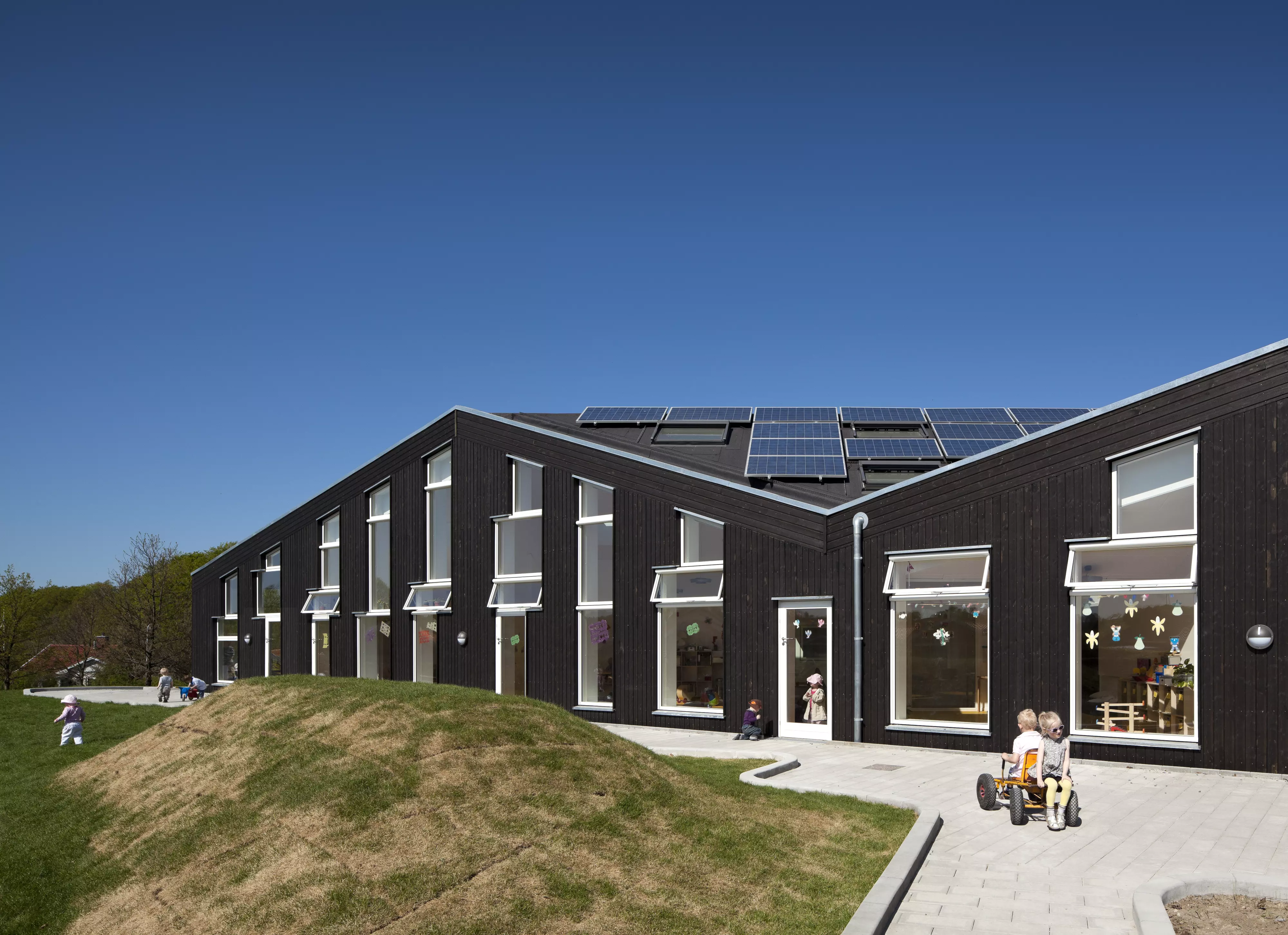 Daycare facility with solar panels, large windows, and outdoor play area.