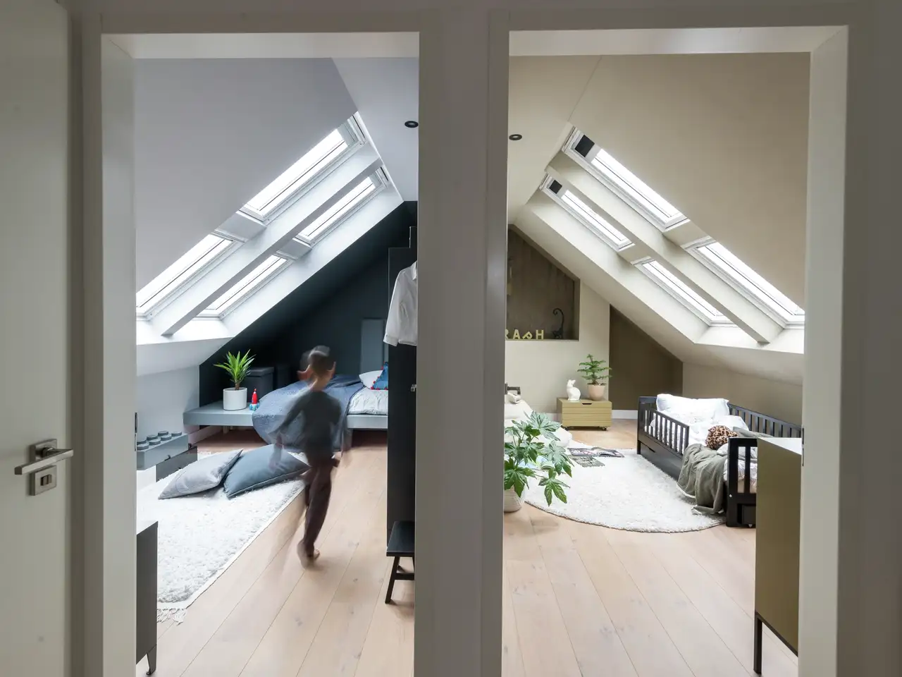 Zolder-kinderkamer met schuine plafonds en VELUX dakramen, kind aan het spelen.