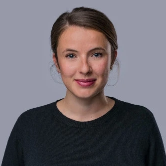 Person in dark sweater against plain grey background, upper body portrait.
