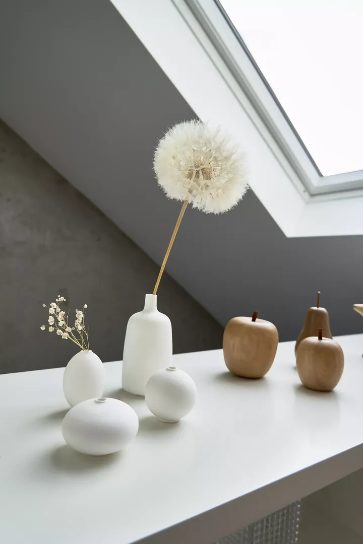 Minimalistische Vasen und hölzerne Äpfel auf einem Tisch unter einem VELUX Dachflächenfenster.