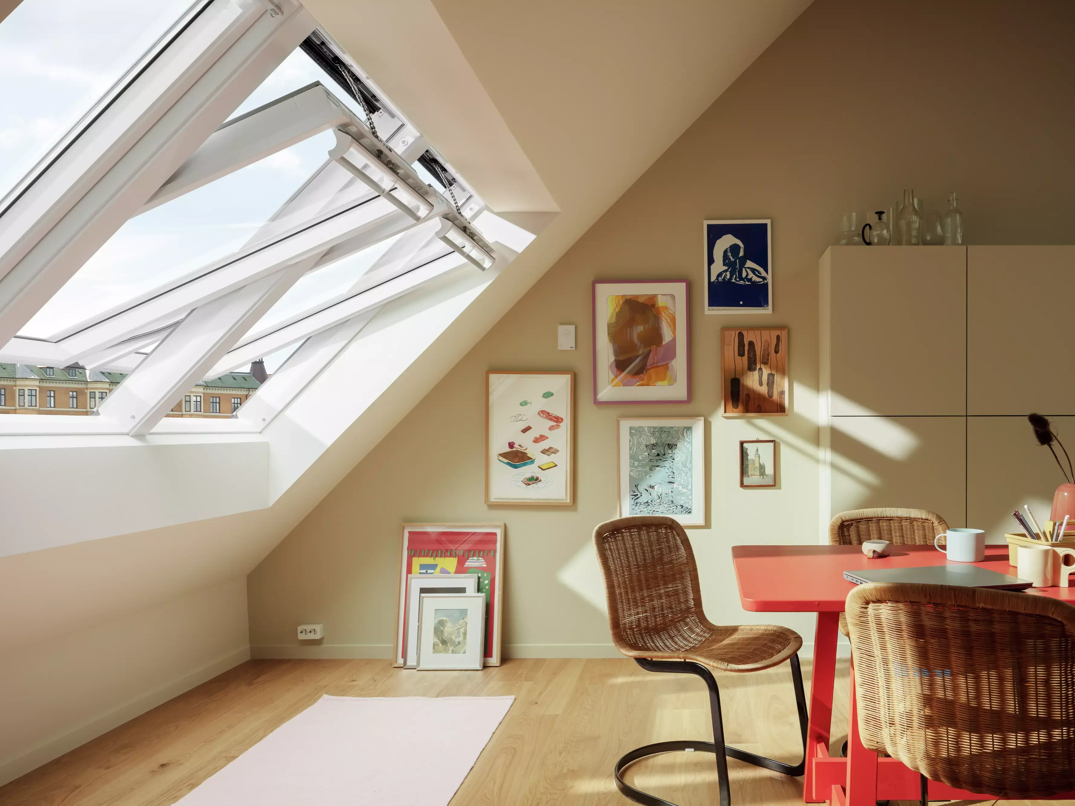 Bureau à domicile de type loft avec fenêtres VELUX, décoration artistique et bureau rouge.