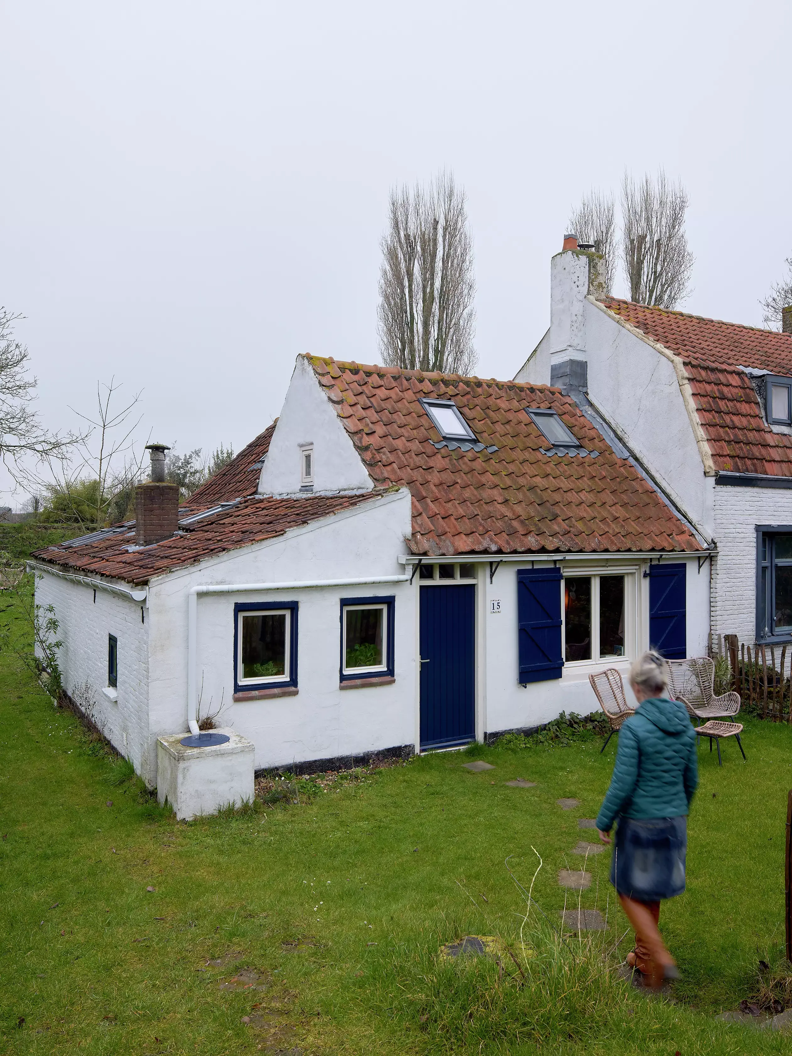 Cottage de campagne avec fenêtre de toit VELUX et une femme qui passe devant.
