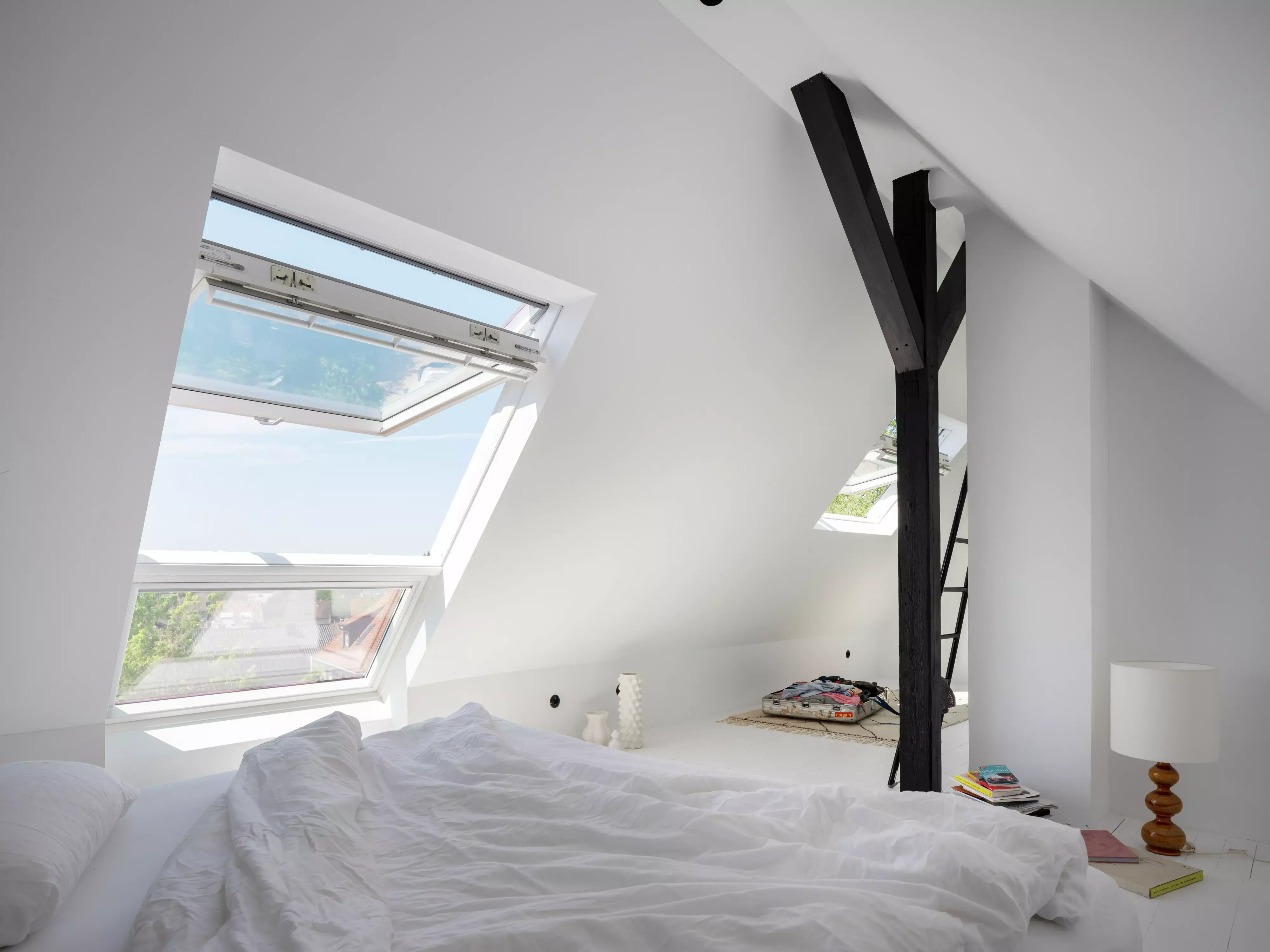 Chambre de comble minimaliste avec un lit et deux fenêtres de toit VELUX ouvertes montrant le ciel bleu.