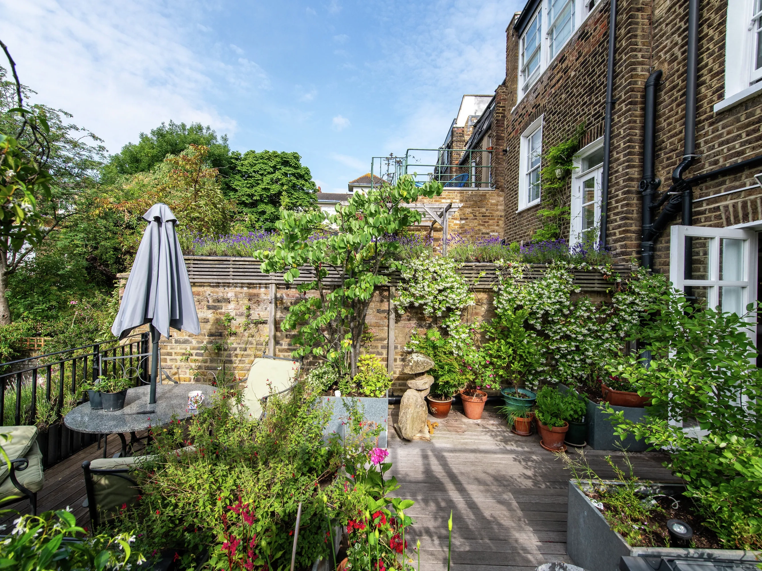Terraza de vivienda con plantas, árboles y arbustos y zona de comedor exterior con sombrilla