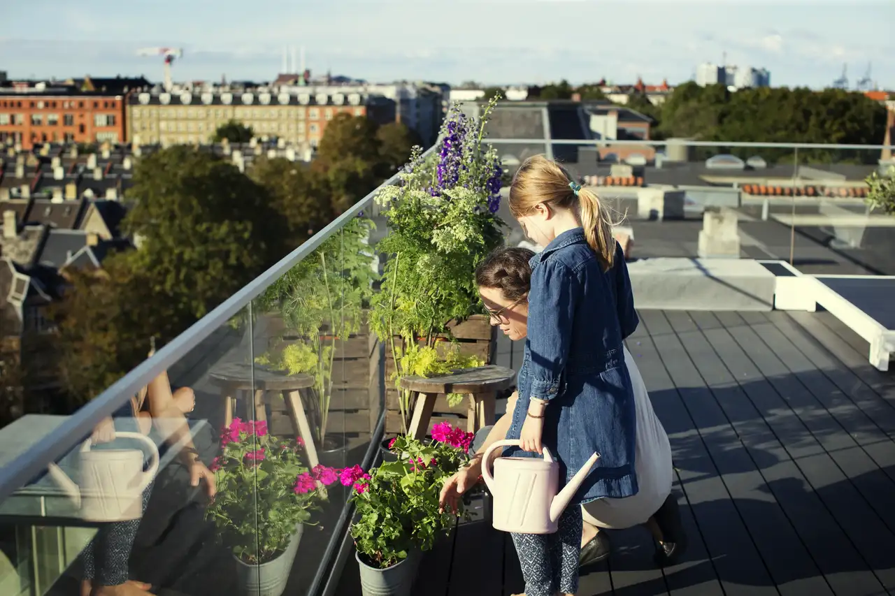 Une femme et une fillette arrosent des plantes en pot sur une terrasse.