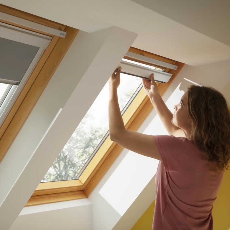 Person adjusting VELUX roof window in a bright attic room with yellow walls.