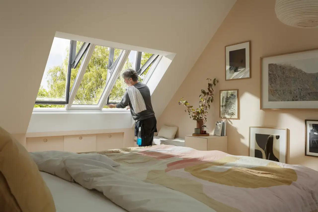 A man cleans VELUX roof windows by activating the windows' tilt function