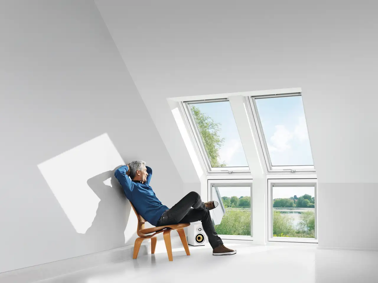 Un homme profite de la vue et de la lumière du soleil assis devant deux fenêtres de toit VELUX