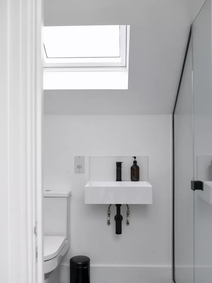 Modernes Badezimmer innen mit natürlichem Licht von einem VELUX Dachflächenfenster, weißem Waschbecken und Spiegel.