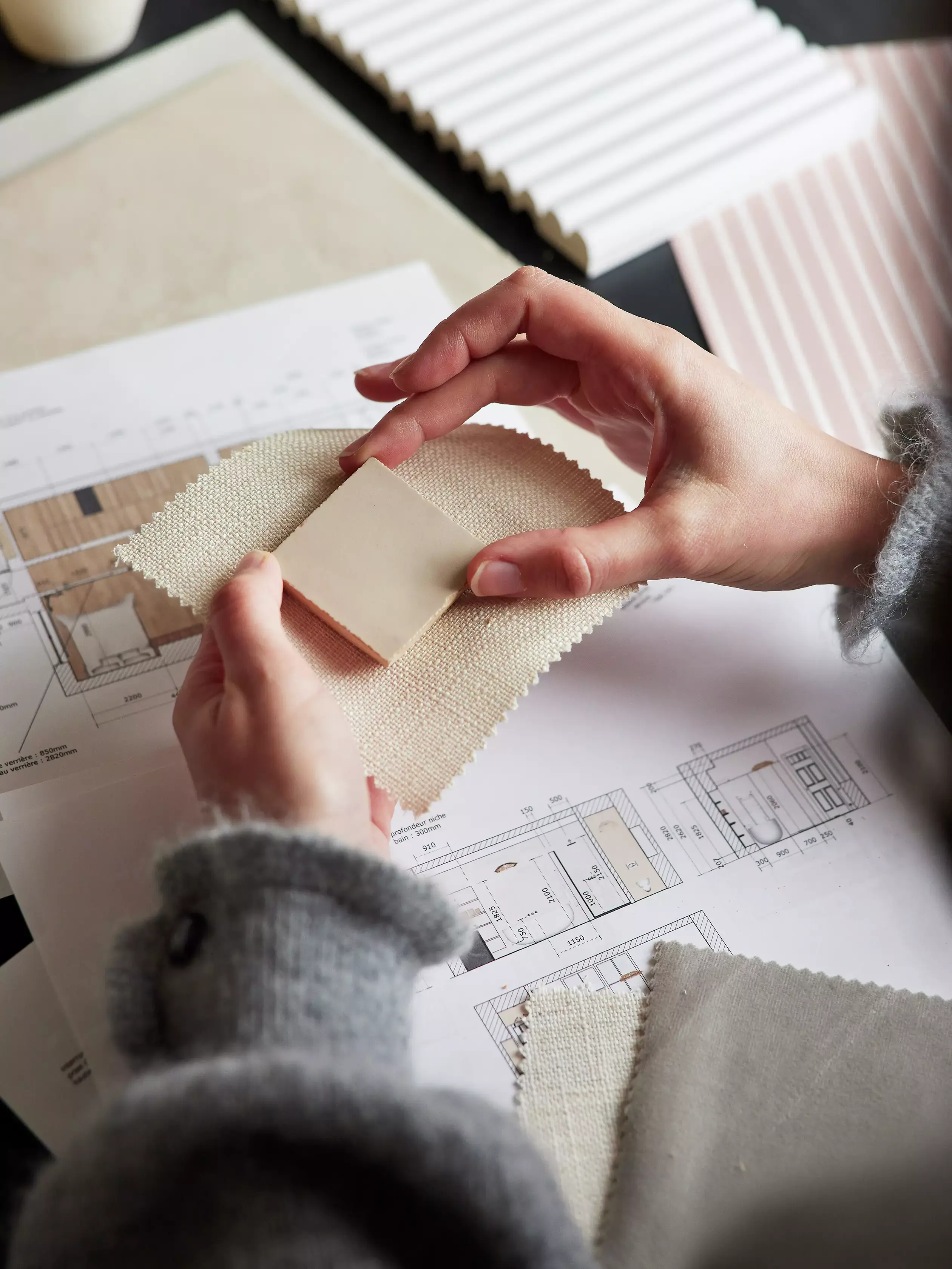 Primo piano di mani che confrontano campioni di tessuto su progetti per il design d'interno.